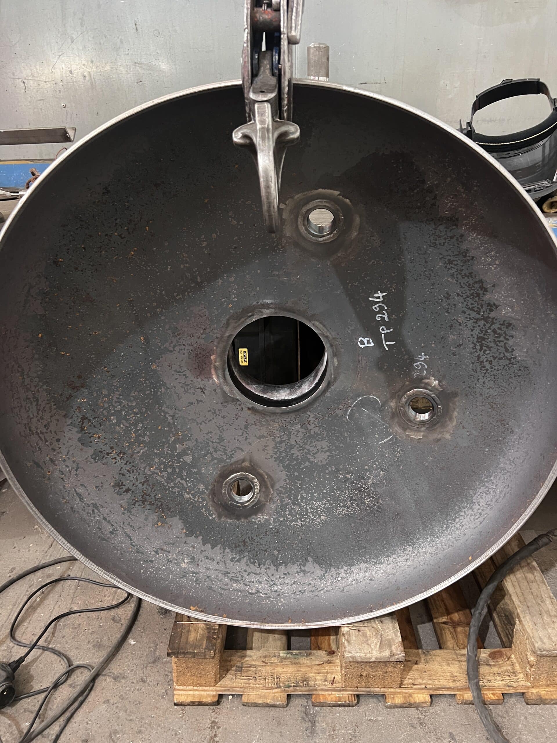 Disque en acier industriel percé avec marquage B TP 294, suspendu par une pince dans un atelier de fabrication métallique.