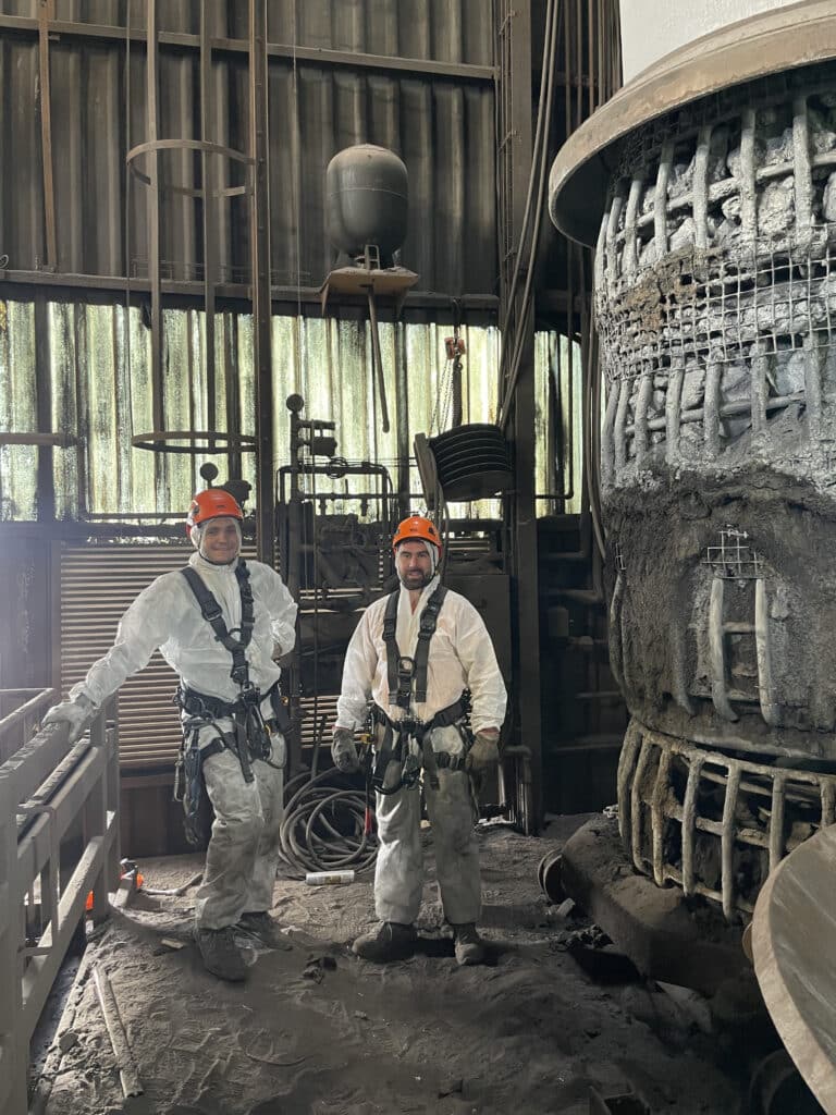 Maintenance industrielle : techniciens en tenue de sécurité Techniciens souriants en harnais de sécurité devant une imposante installation industrielle en maintenance.