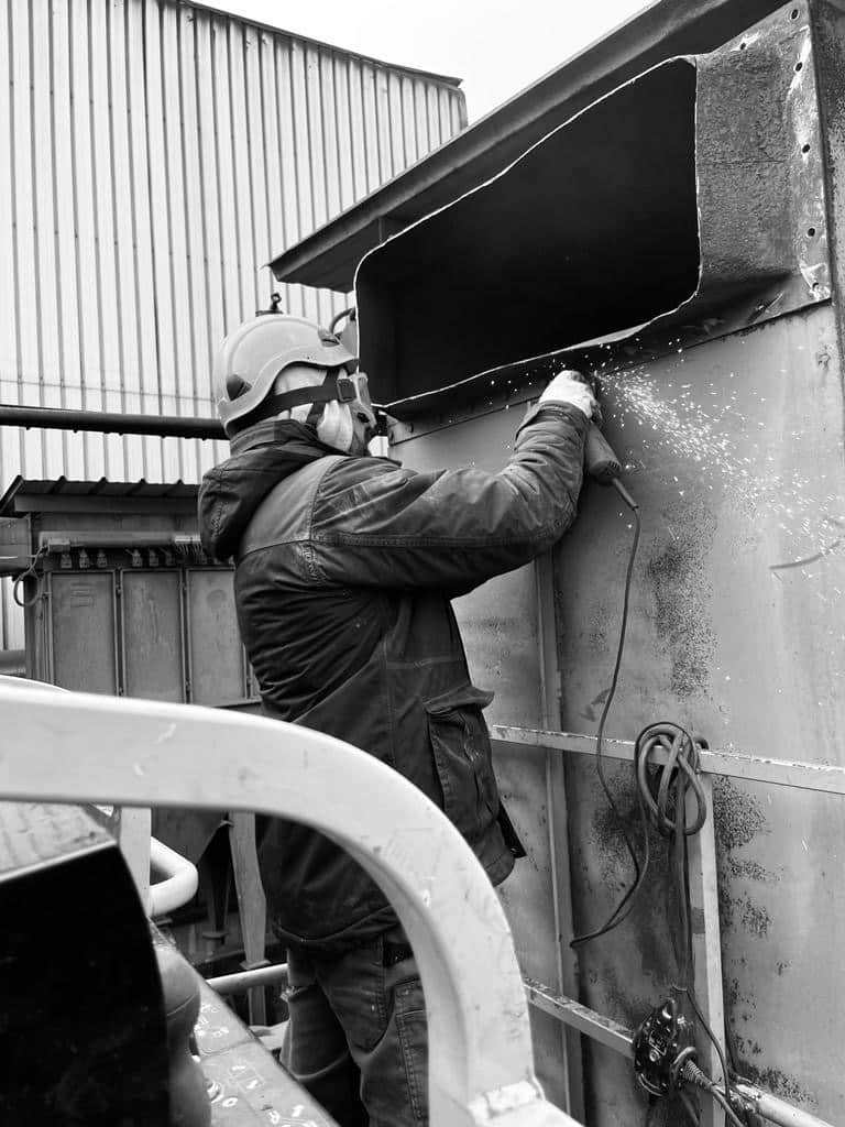 Travaux de Meulage Industriel : Un Ouvrier en Action Ouvrier équipé meulant une structure métallique industrielle, étincelles jaillissantes lors de la découpe.