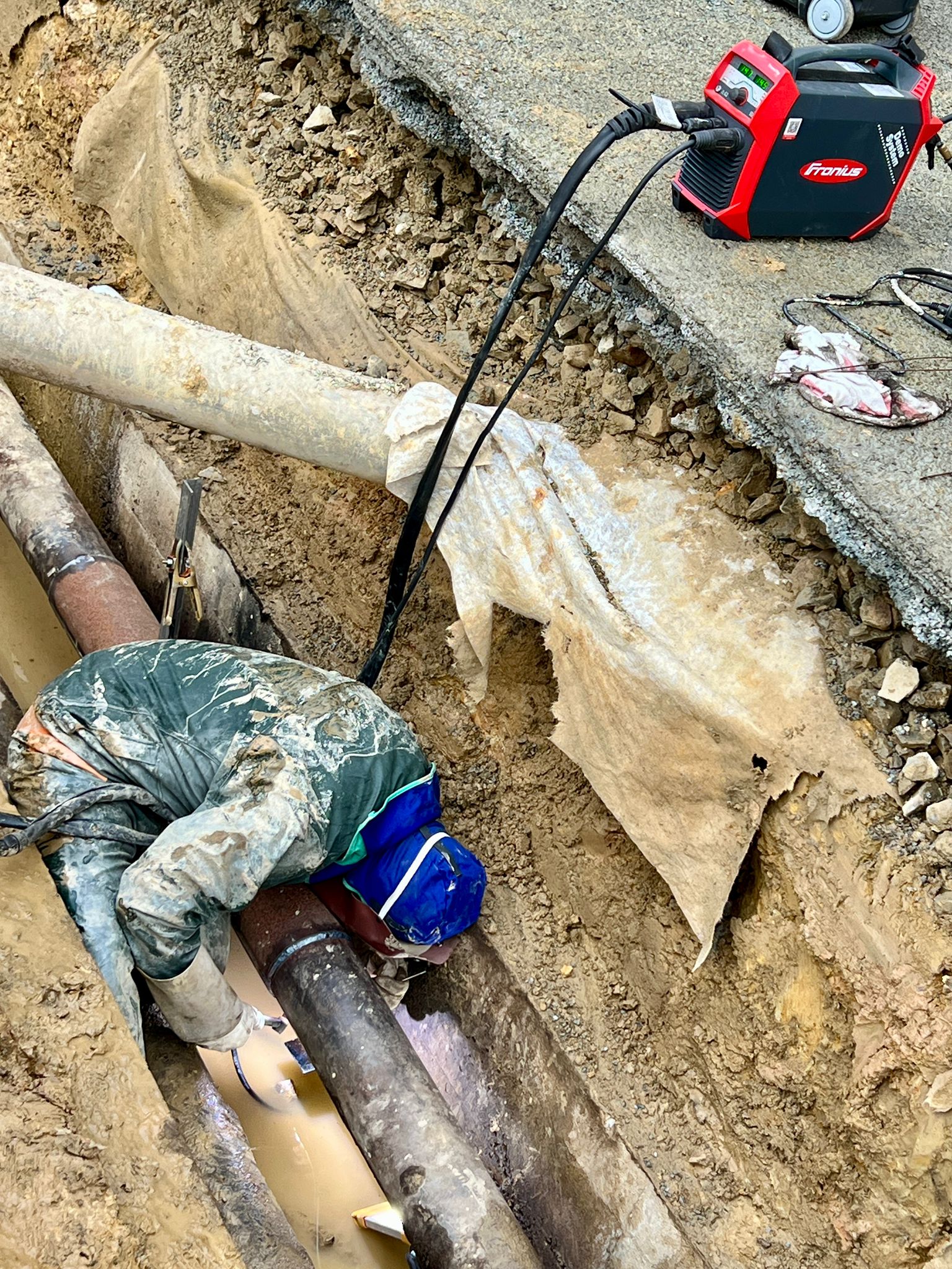 Soudeur travaillant sur un pipeline dans une tranchée humide avec un poste à souder Fronius.
