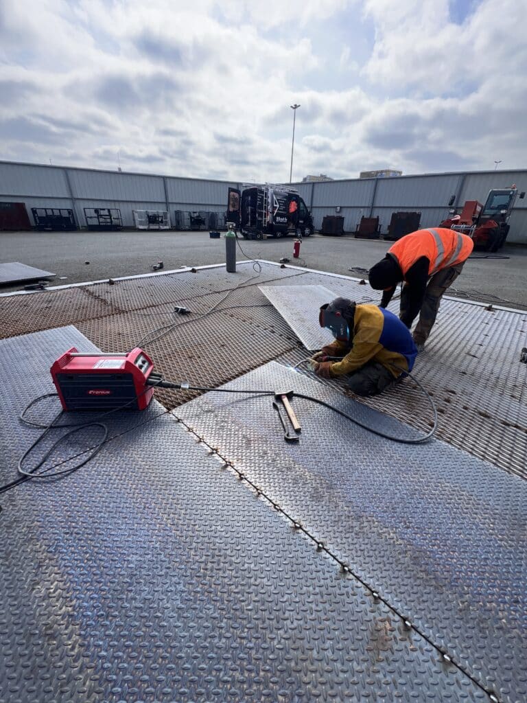 Soudure industrielle de tôle damier sur chantier extérieur Soudeurs assemblant des plaques métalliques avec un poste Fronius en extérieur. Van 89art.fr en arrière-plan.